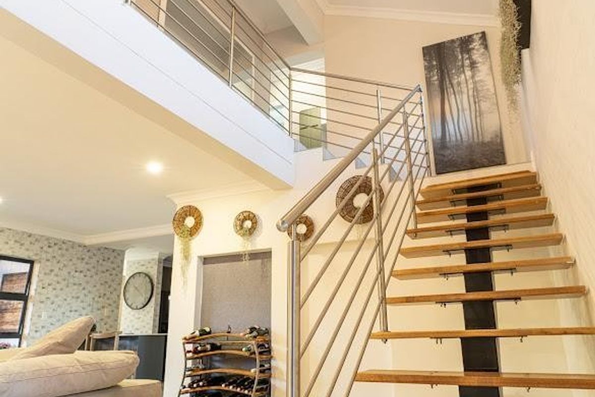 Modern open-plan living area featuring a striking staircase with wooden treads and a stainless steel balustrade leading to a mezzanine level.
