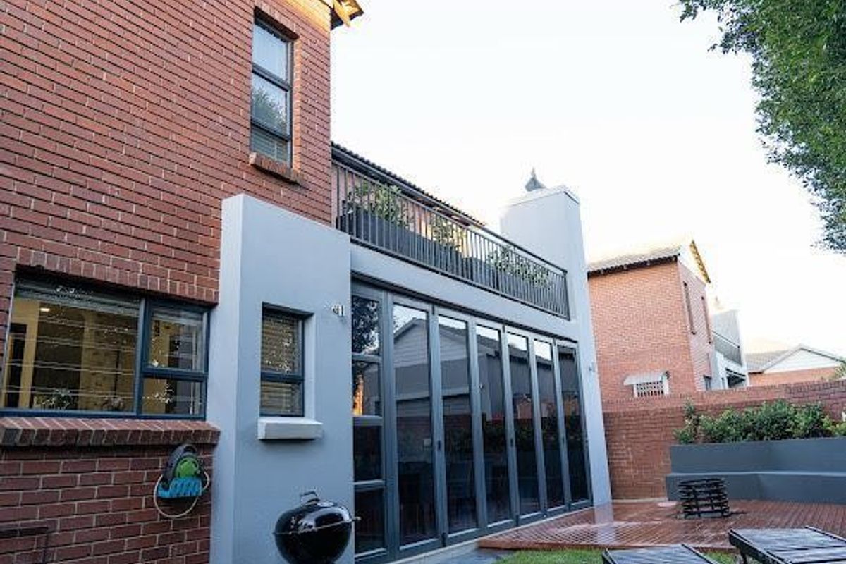 Rear view of a townhouse featuring a brick and stucco facade, large folding glass doors, a balcony with metal railing, and a timber deck.