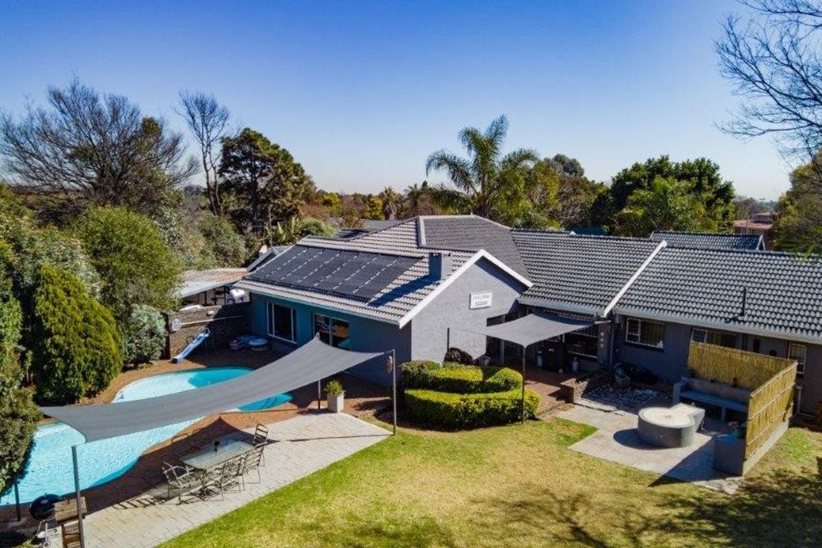 Aerial view of a residential property featuring a tiled roof with solar panels, a swimming pool, paved patio area, and a landscaped garden.