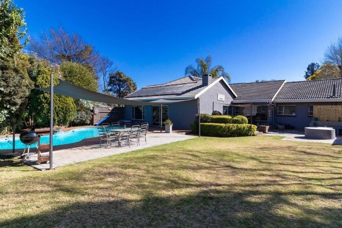 Spacious rear garden featuring a swimming pool, paved patio area, and well-maintained lawn, ideal for outdoor entertaining.