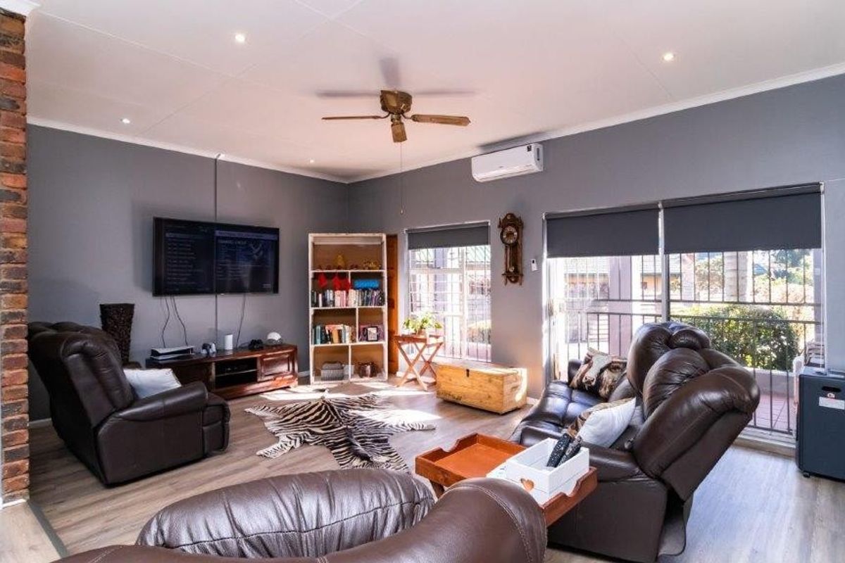 Spacious living room featuring laminate flooring, exposed brick accents, a ceiling fan, and split-system air conditioning with direct access to an outdoor area.