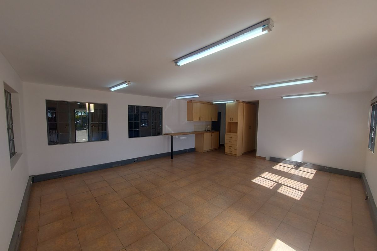 Spacious open-plan industrial office or utility area featuring tiled flooring, built-in cabinetry, and ample natural light through steel-framed windows.