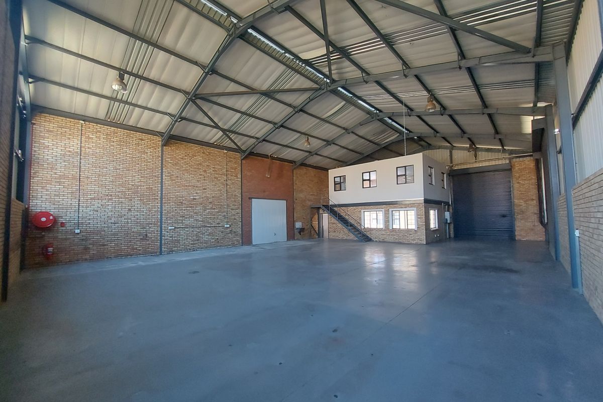 Spacious industrial warehouse featuring high-clearance steel truss roofing, polished concrete floors, exposed brickwork, and an integrated mezzanine office level with a roller shutter door.