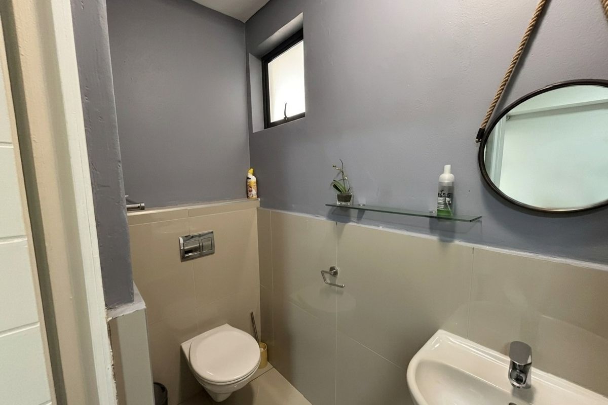 A compact modern bathroom featuring a wall-mounted toilet with a concealed cistern, a ceramic washbasin with chrome fittings, and neutral wall tiling.