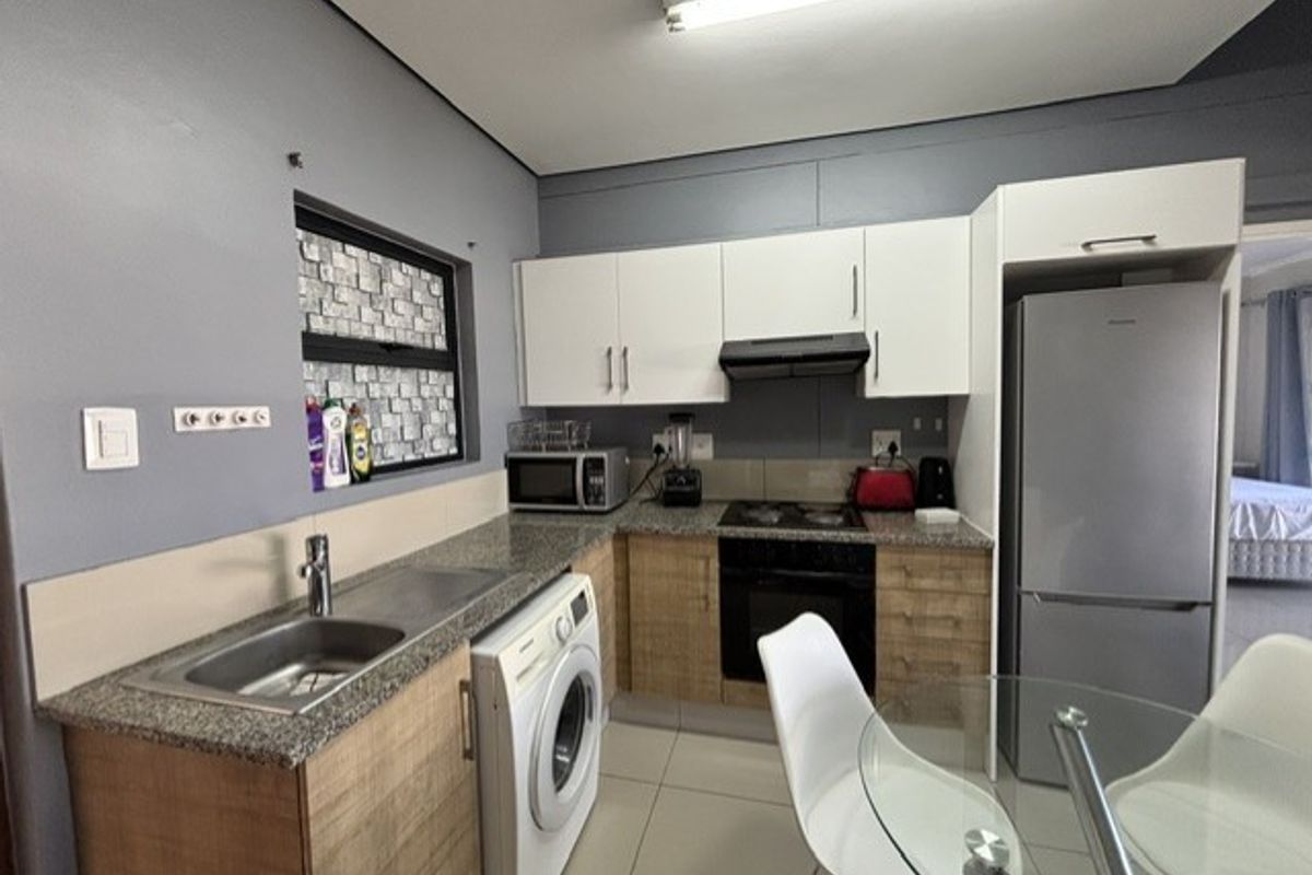 Compact kitchen featuring modern white and wood-tone cabinetry, granite countertops, integrated appliances, and tiled flooring, offering a functional and efficient workspace.