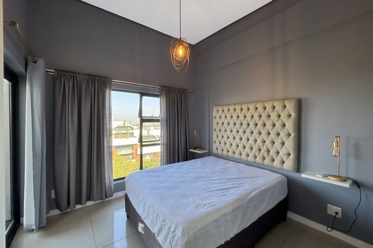 A modern bedroom featuring tiled flooring, a neutral color palette, and large windows providing natural light and urban views.