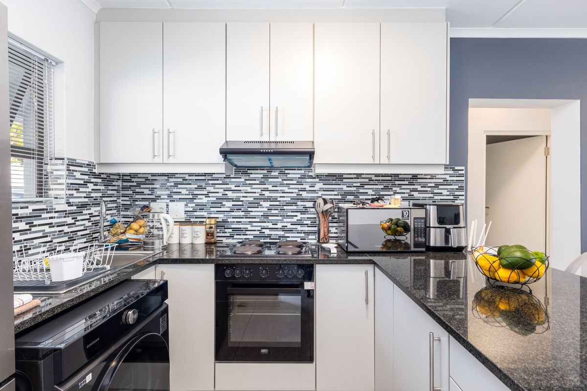 Modern kitchen featuring white cabinetry, granite countertops, a mosaic tile backsplash, and integrated appliances including an oven and hob.