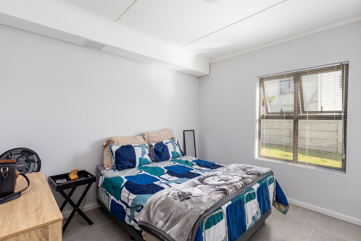 A bright bedroom featuring neutral tiled flooring, clean white walls, and an aluminium-framed window with fitted venetian blinds.