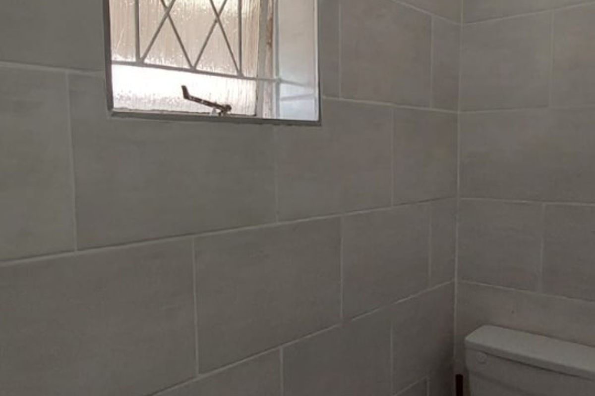 A compact bathroom featuring neutral wall tiling, a standard toilet, and a small window with a security grille.