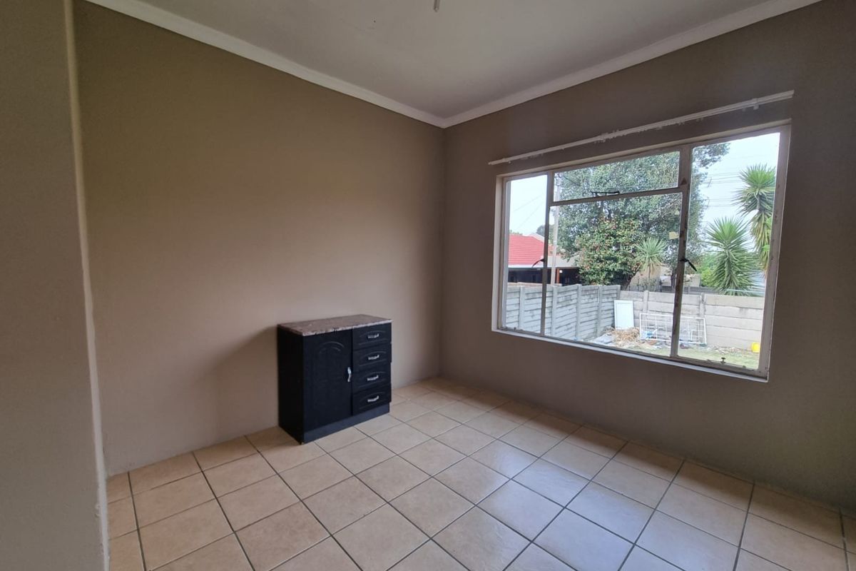 A simple, neutrally painted bedroom featuring tiled flooring and a large window that provides natural light.