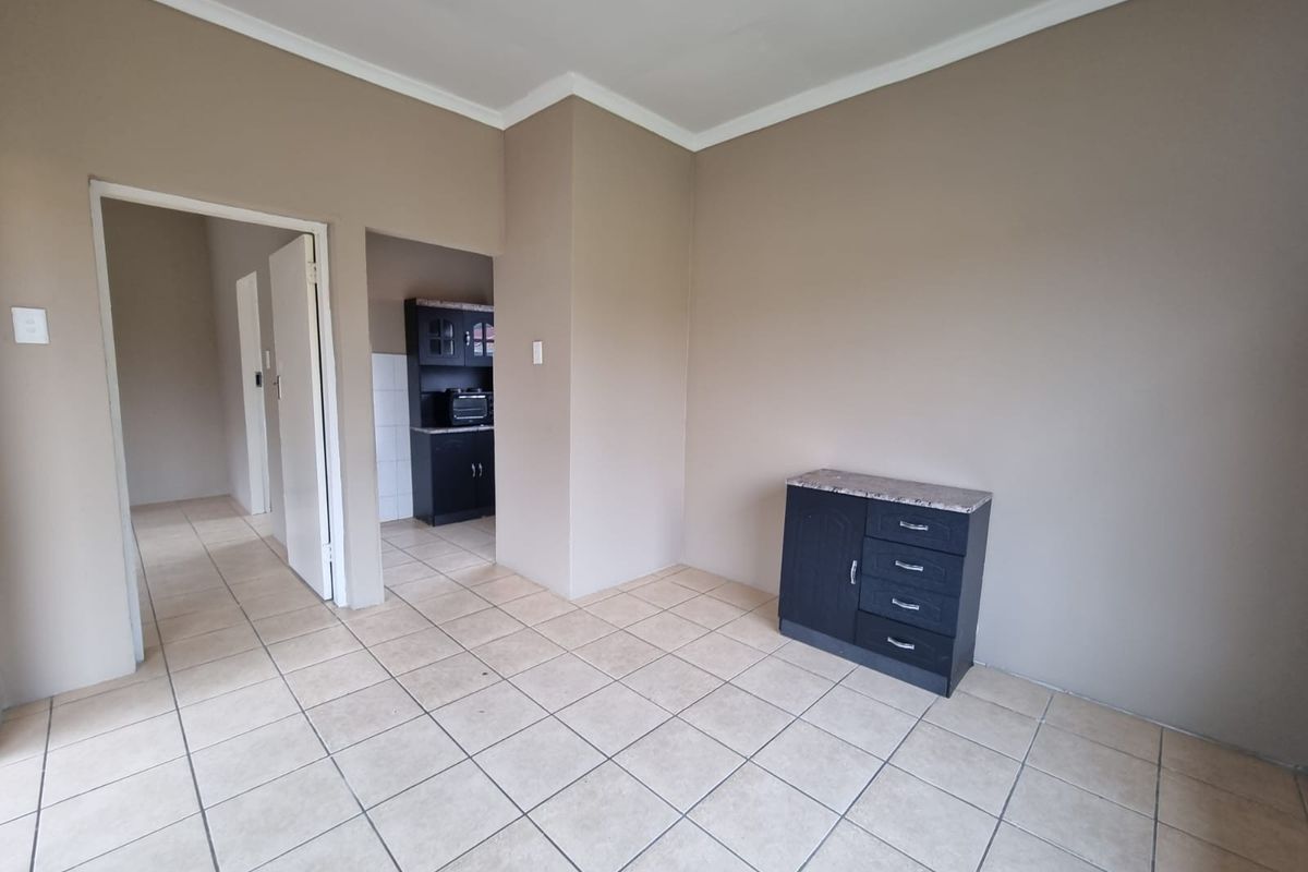 A spacious living area featuring neutral wall tones, tiled flooring, and a coved ceiling, with an adjacent view into the kitchen area.