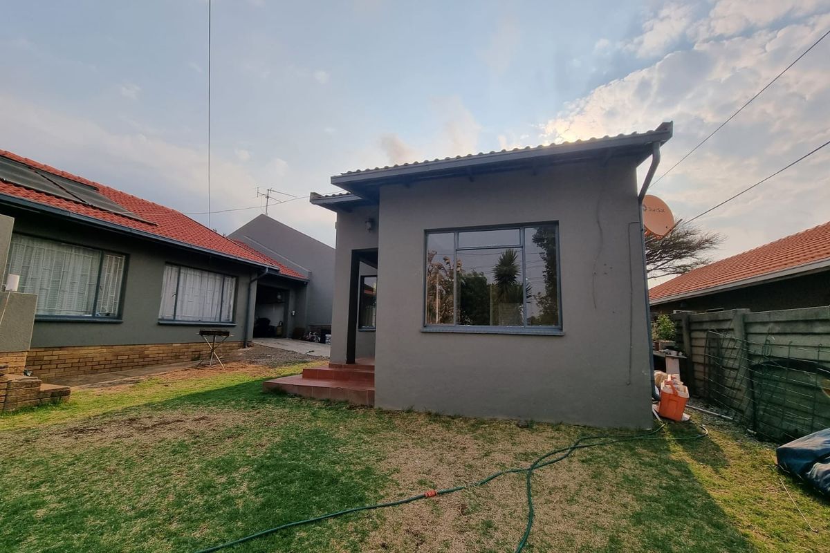 Rear view of the townhouse featuring a grey rendered facade, tiled roof, and a small lawn area.
