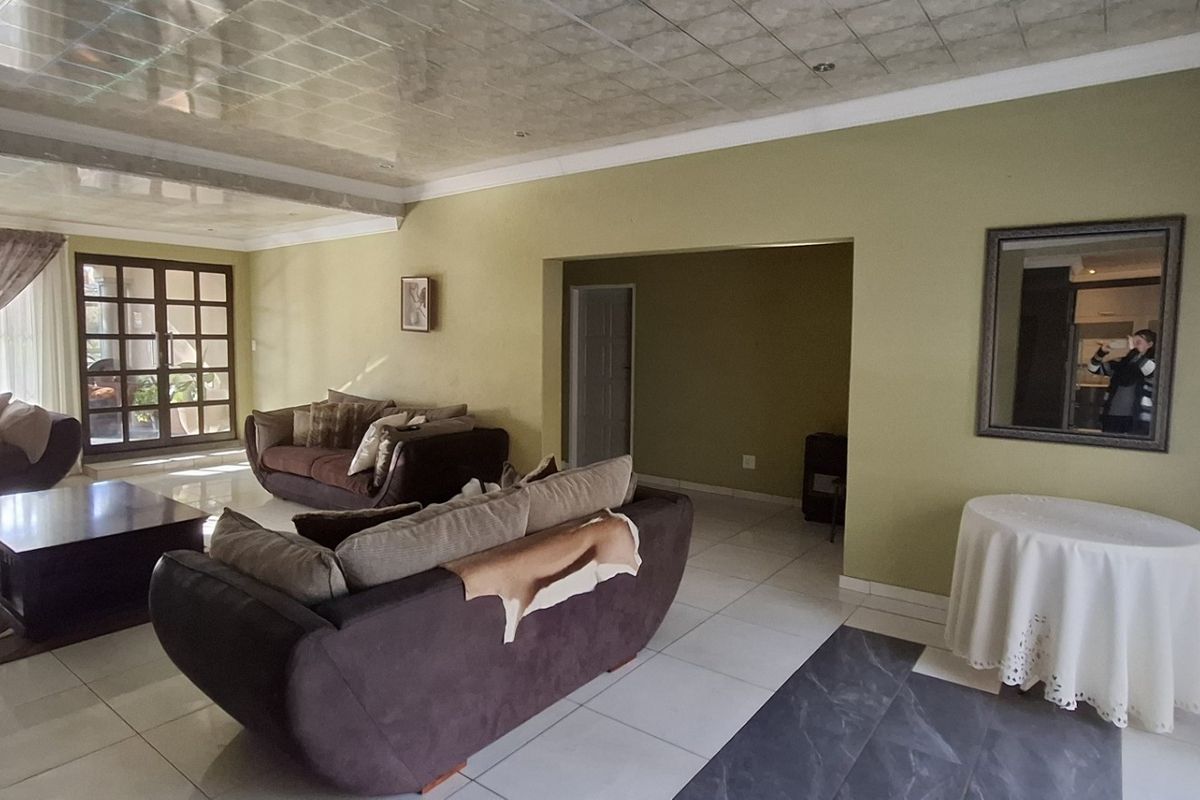Spacious living area featuring tiled flooring, recessed lighting, and a distinctive grid-pattern ceiling, offering a functional layout with access to adjacent rooms.