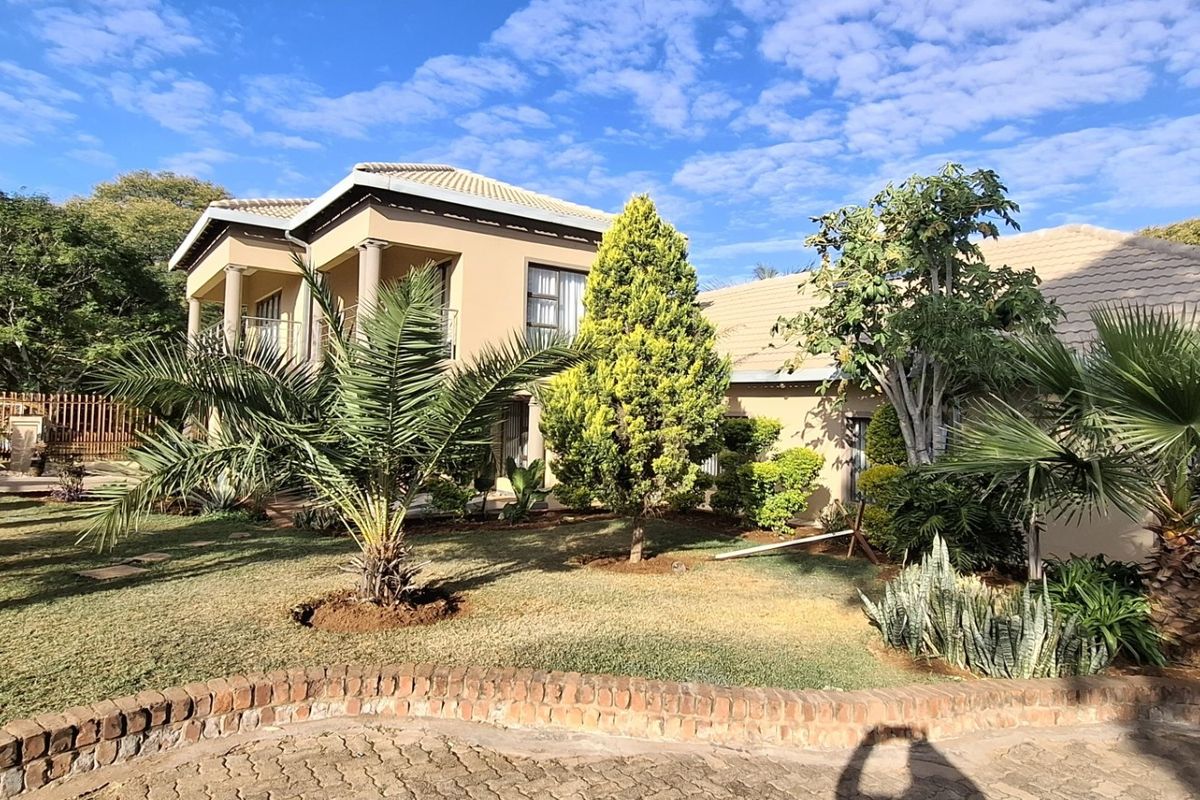 Rear view of a two-story residential property featuring a landscaped garden, brick paved driveway, and a balcony with structural columns.