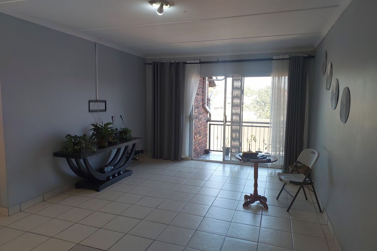 A living room featuring tiled flooring and a sliding glass door leading to a balcony, providing natural light and access to outdoor space.