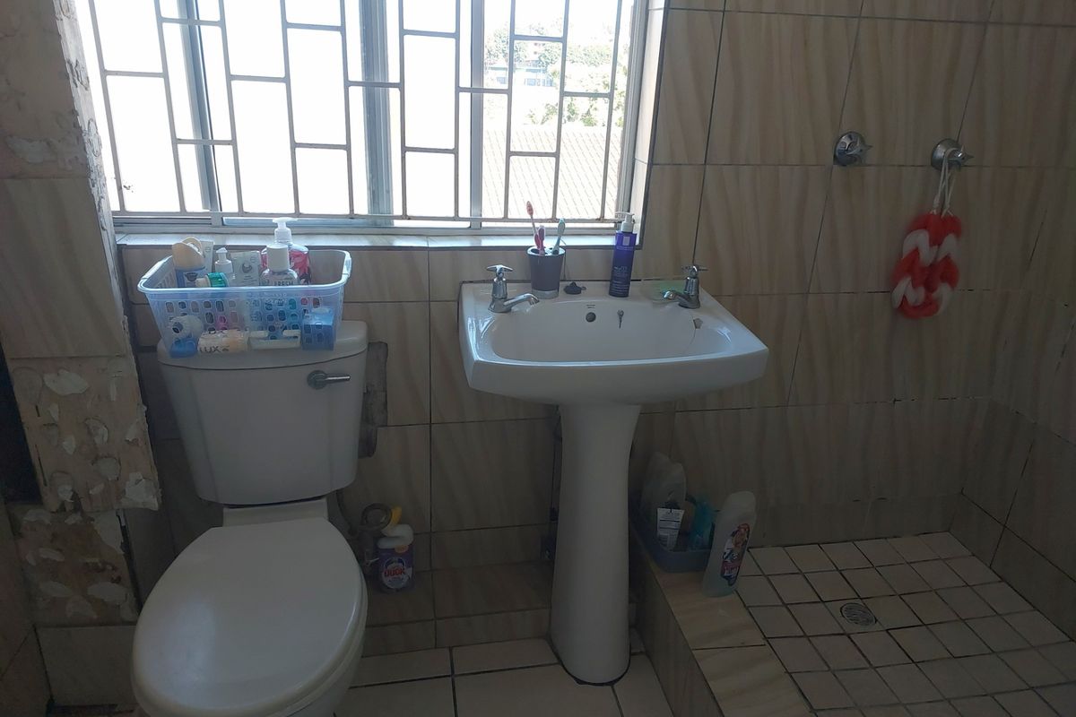 A functional bathroom featuring a pedestal basin, toilet, and shower area with tiled finishes, requiring cosmetic updates to improve its overall condition.