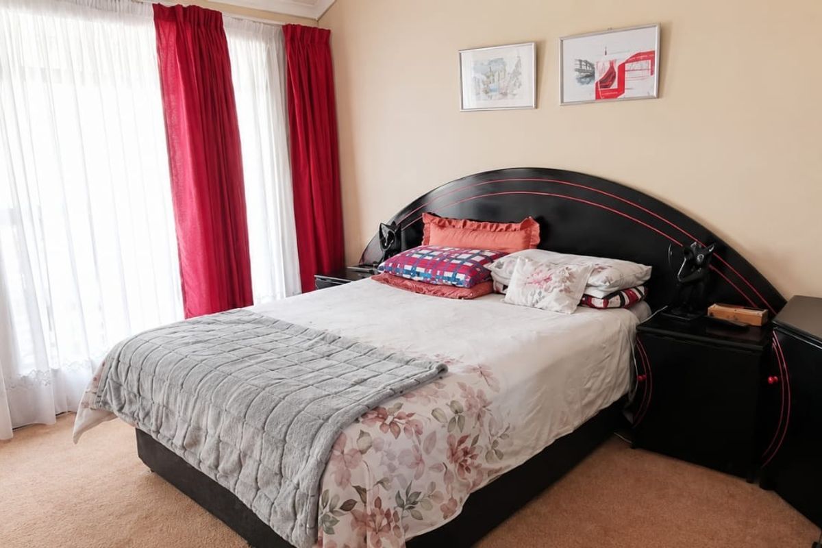A well-lit bedroom featuring neutral wall tones, carpeted flooring, and large windows with curtain tracks.