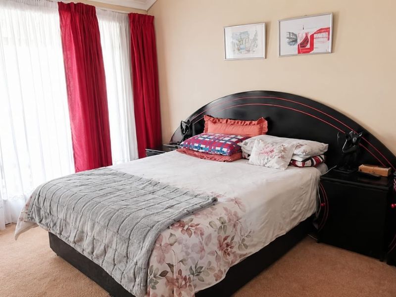 A well-lit bedroom featuring neutral wall tones, carpeted flooring, and large windows with curtain tracks.