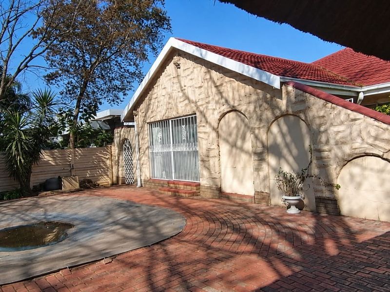 Rear exterior view featuring a brick-paved patio area, a swimming pool with a cover, and a stone-clad building facade under a tiled roof.
