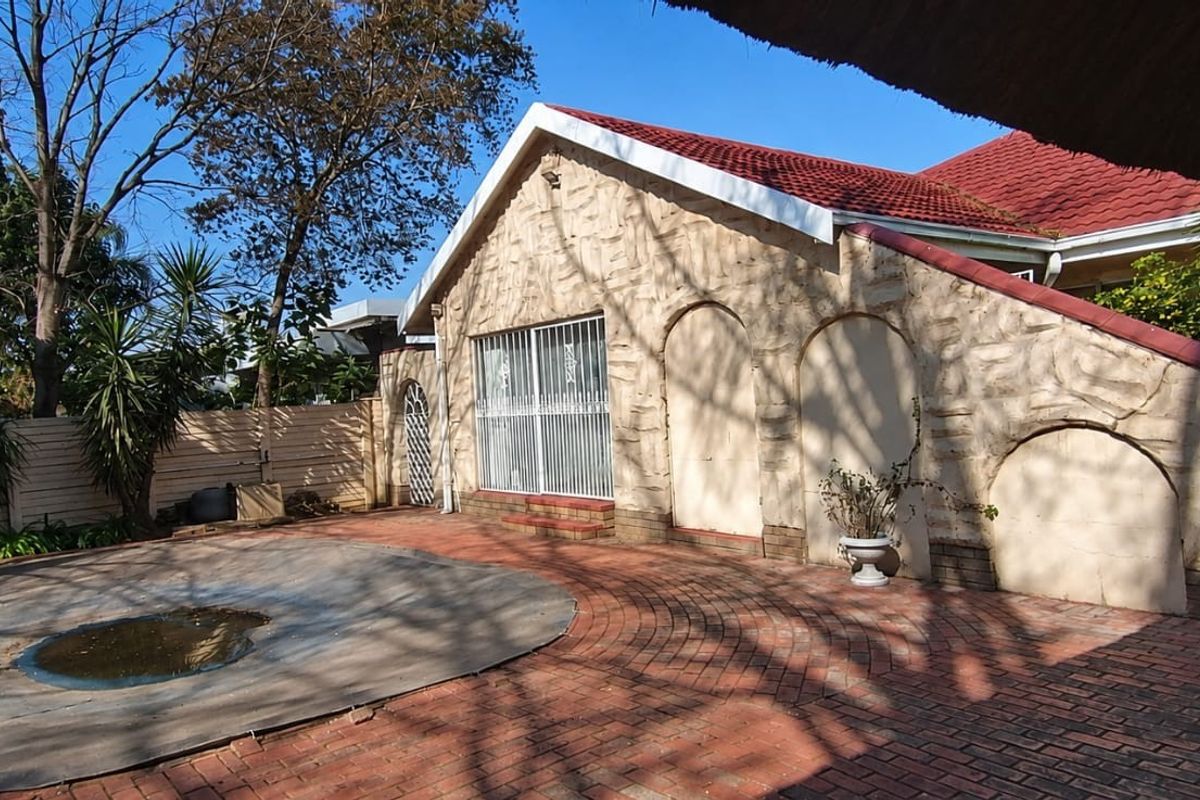 Rear exterior view featuring a brick-paved patio area, a swimming pool with a cover, and a stone-clad building facade under a tiled roof.