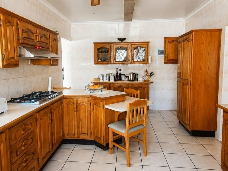 A traditional kitchen featuring extensive wooden cabinetry, a gas hob with extractor, built-in double oven, and tiled flooring throughout.