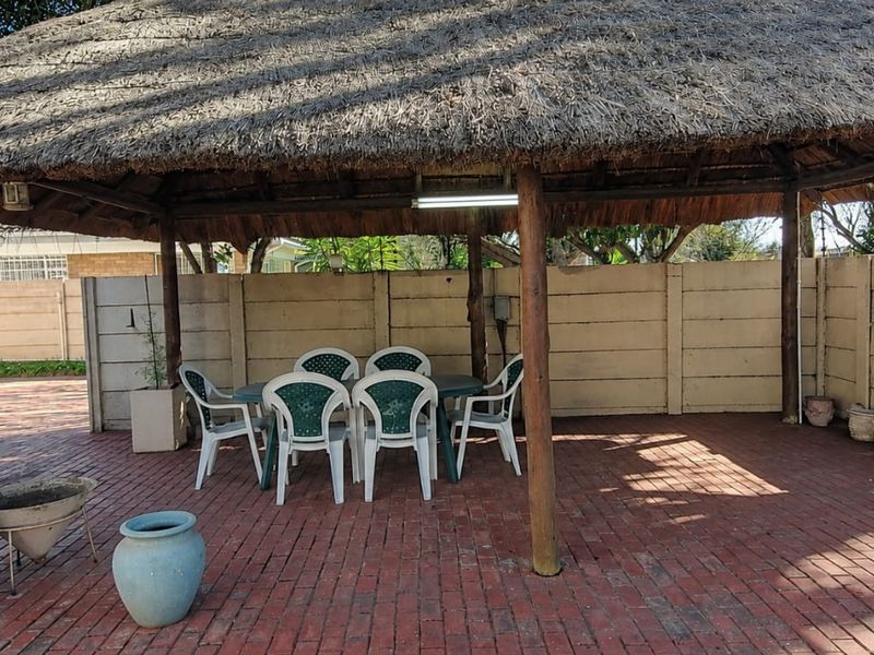 Covered outdoor patio area featuring a traditional thatched roof, timber support posts, and brick paving, enclosed by a precast concrete boundary wall.