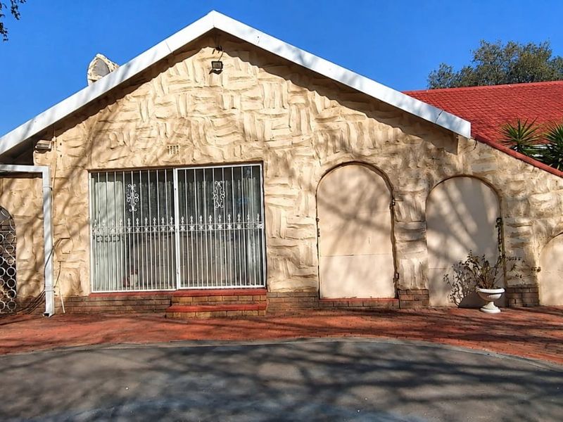 Front elevation of a house featuring a unique stone-clad facade, arched entryways, a sliding glass door with security bars, and a brick-paved driveway.