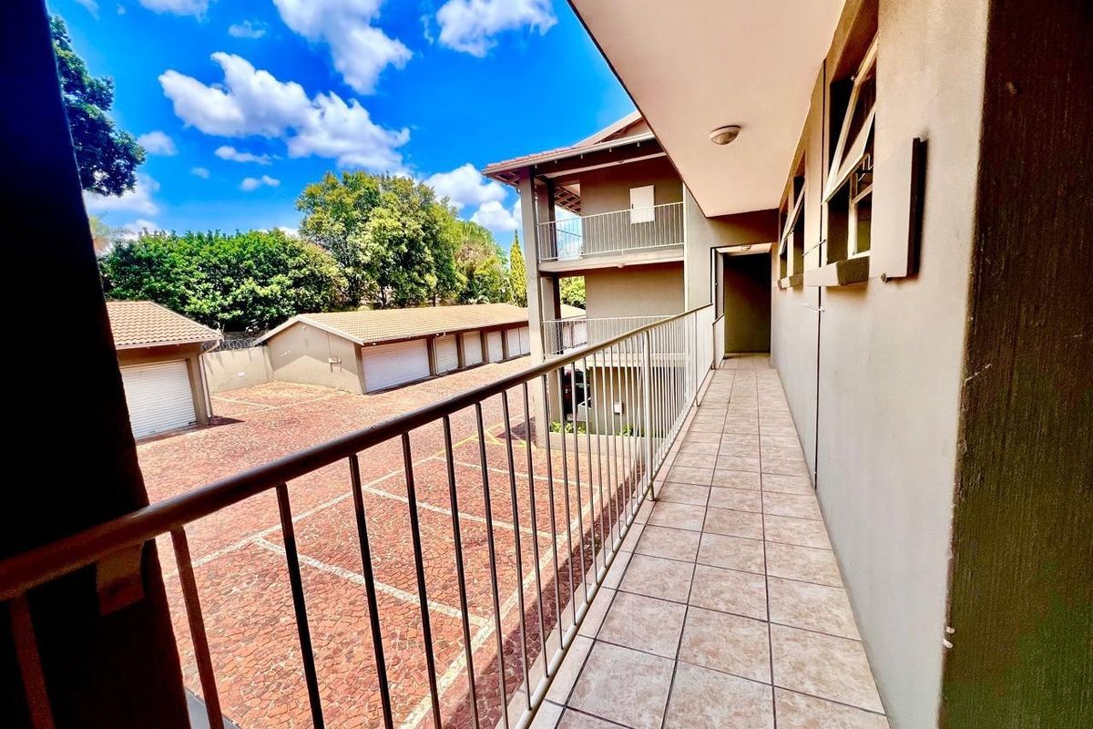 An elevated exterior walkway or balcony featuring tiled flooring and a metal safety railing, overlooking the apartment complex parking area.