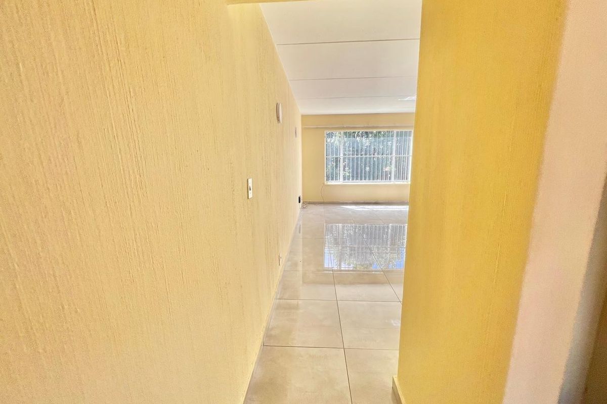 An empty, bright living area featuring large windows with security bars and polished tiled flooring, offering a clean and neutral space.