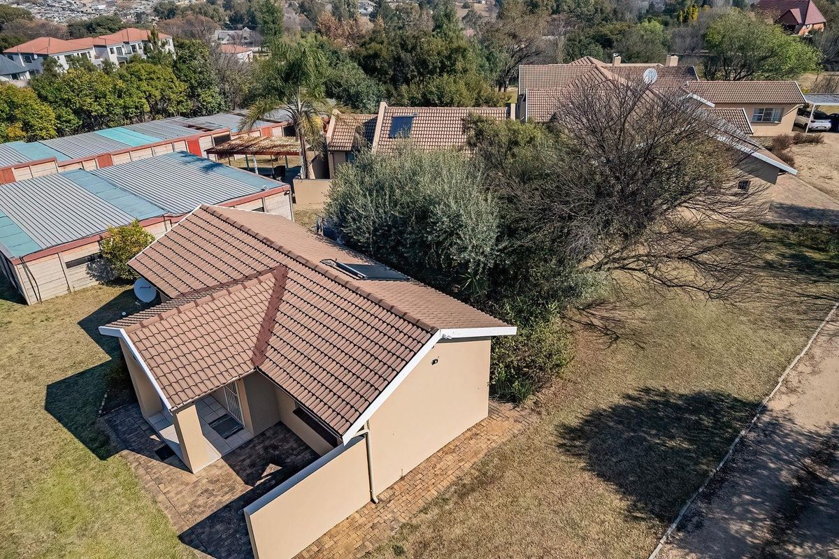 Aerial view of the property showing the main house with a tiled roof, solar water heater, and surrounding grounds with paved driveway and boundary walls.