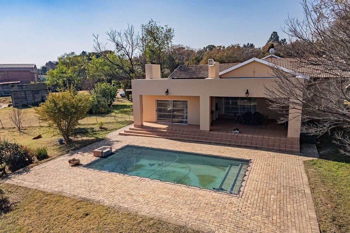 Aerial view of the rear exterior featuring a covered patio, brick-paved pool deck, and a swimming pool set within a spacious garden.