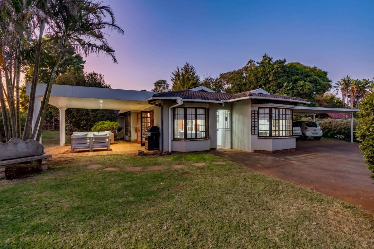 Rear view of the house featuring a covered patio area, paved driveway, carport, and classic bay windows set in a landscaped garden.