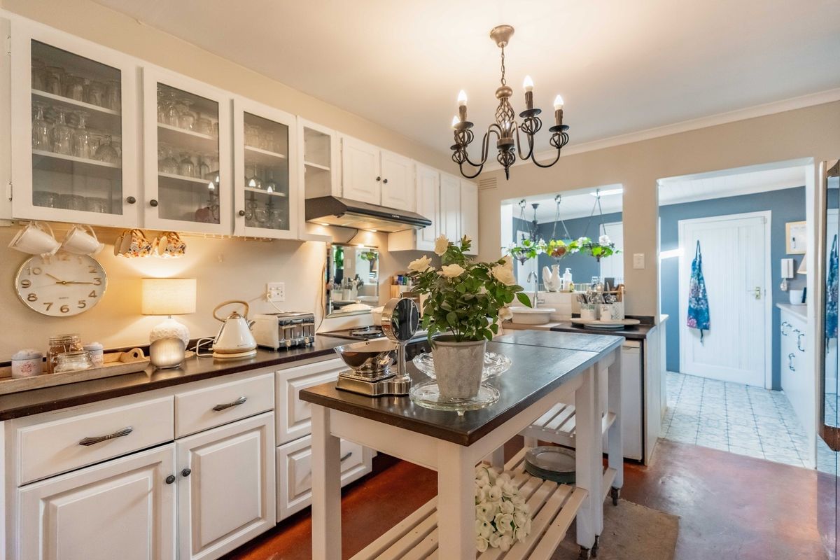 A well-maintained kitchen featuring white cabinetry, dark countertops, and a classic chandelier, with an open layout leading to an adjacent utility area.