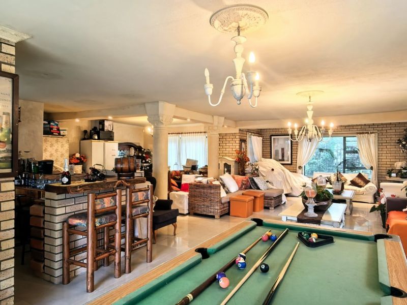 Spacious open-plan living area featuring brick accent walls, decorative ceiling roses, chandeliers, and a built-in bar, offering a versatile layout for entertainment.