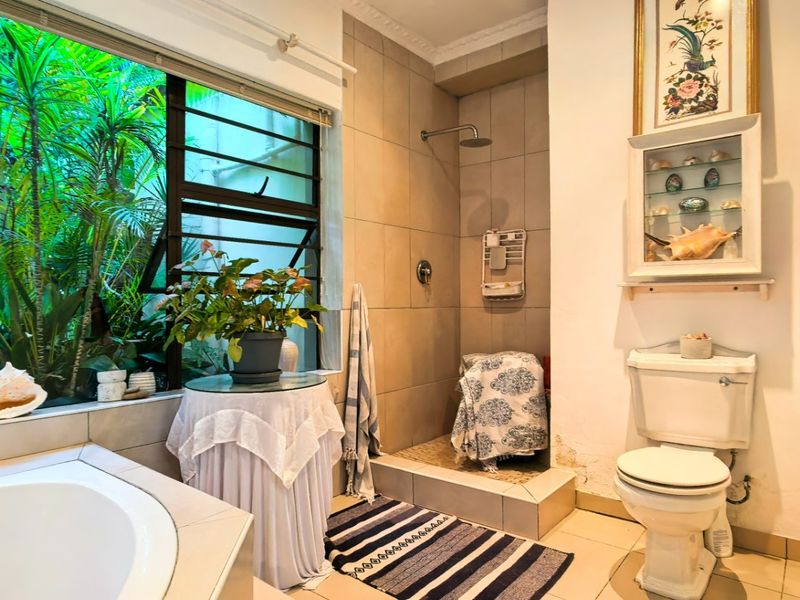 Bathroom featuring a built-in bathtub, walk-in shower with rain head, and large window overlooking a lush garden setting.