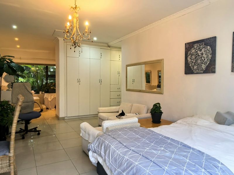 Spacious bedroom featuring tiled flooring, extensive built-in cupboards, decorative coving, and a central chandelier, offering a functional and well-lit living space.