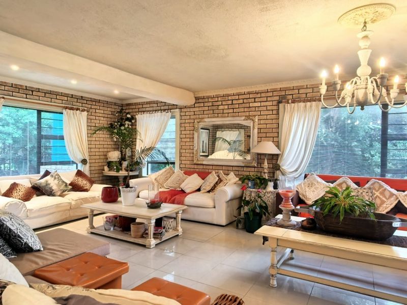Spacious living room featuring exposed brick walls, tiled flooring, and a decorative chandelier, offering a warm and textured aesthetic.