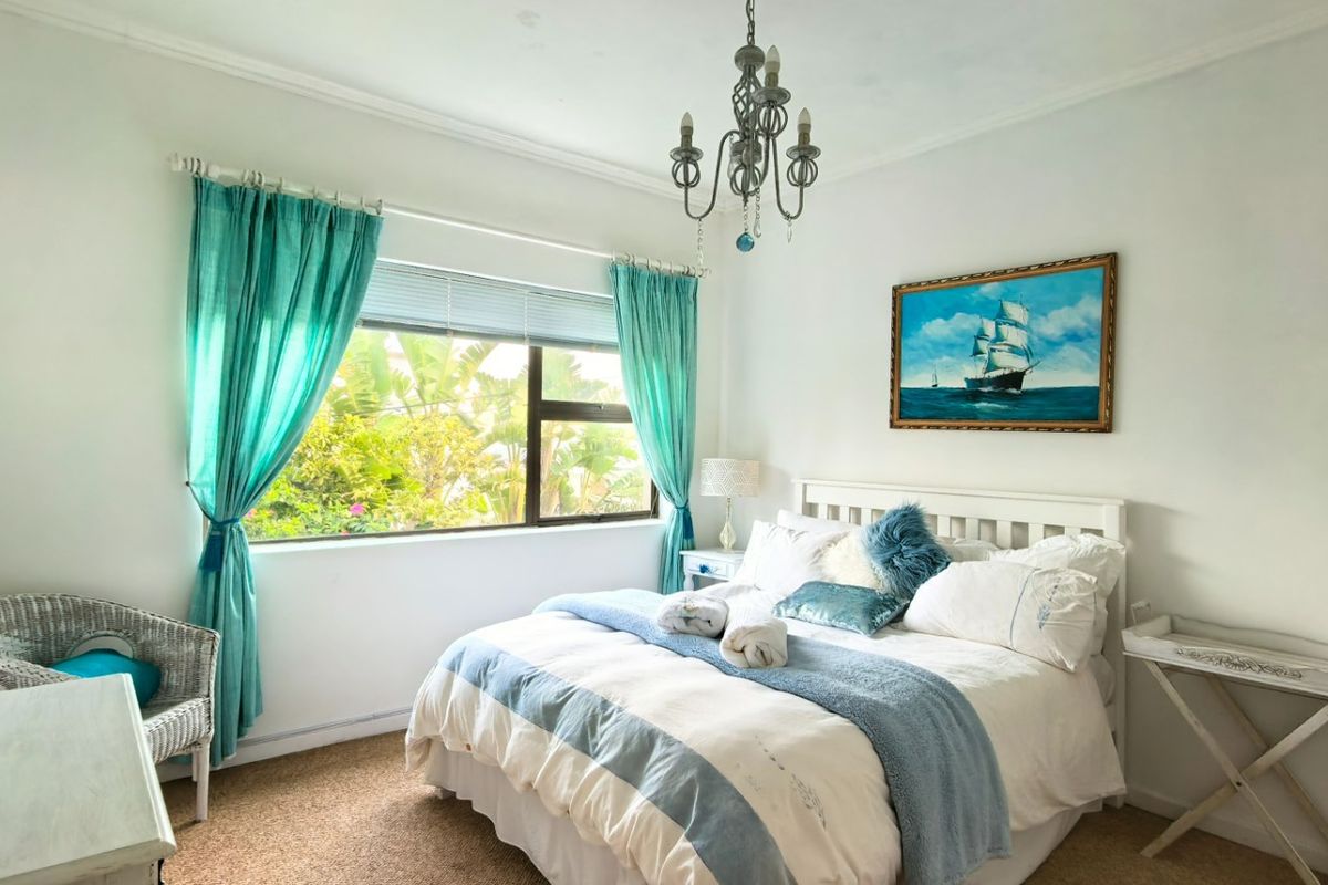 A bright bedroom featuring carpeted flooring, coving, and an aluminium-framed window overlooking the garden.