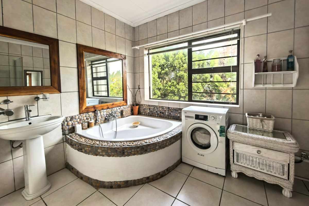 A functional bathroom featuring a corner bathtub with pebble detailing, a pedestal basin, and ceramic tiling throughout, with an integrated laundry appliance space.
