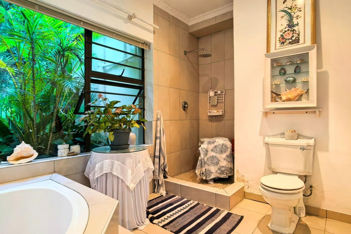 Bathroom featuring a built-in bathtub, walk-in shower with rain head, and large window overlooking a lush garden setting.