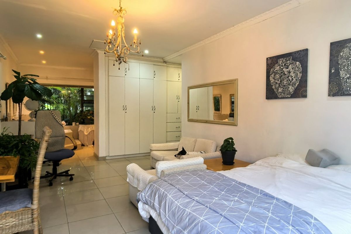 Spacious bedroom featuring tiled flooring, extensive built-in cupboards, decorative coving, and a central chandelier, offering a functional and well-lit living space.