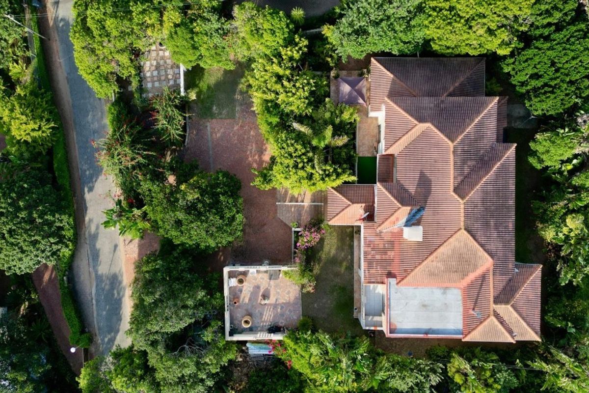 Aerial view of the property showcasing the roof structure, paved driveway, and surrounding landscaped garden areas.