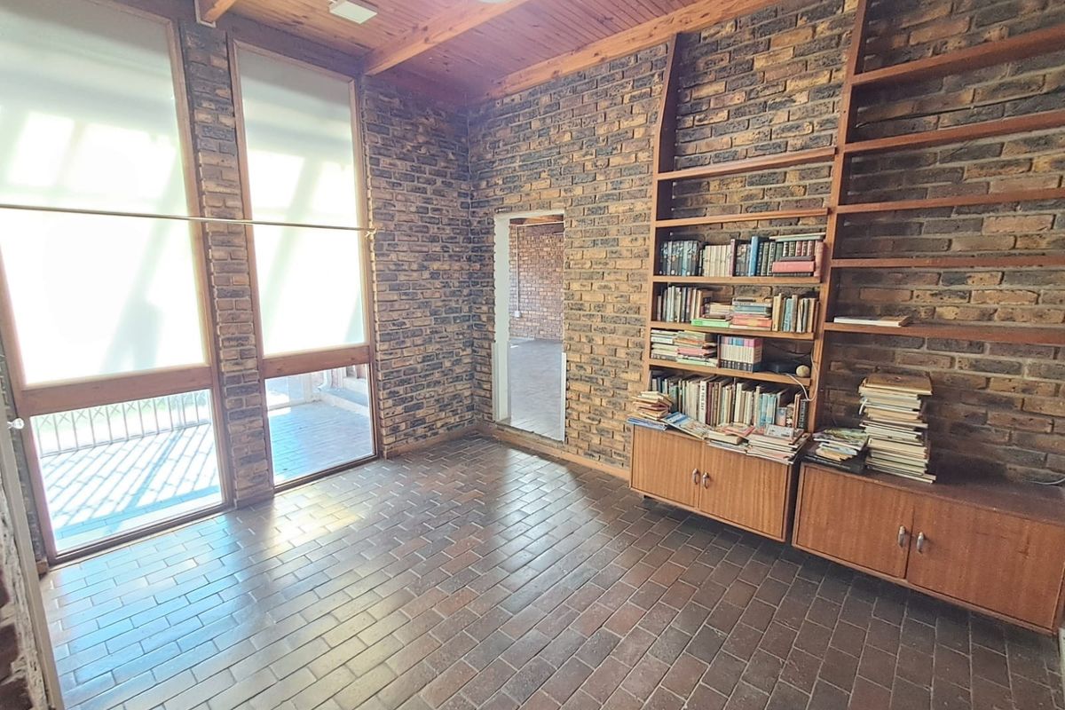A living room featuring exposed brick walls, a timber ceiling, and built-in shelving, with large windows providing natural light and access to the patio.