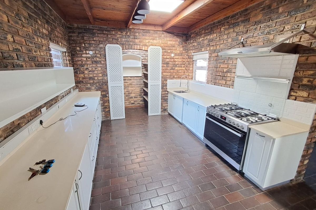 Spacious kitchen featuring exposed brick walls, timber ceiling with skylight, gas stove, extractor fan, and ample built-in cabinetry with tiled flooring.