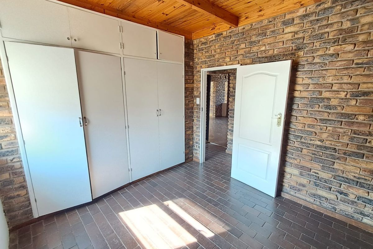 A vacant bedroom featuring facebrick walls, tiled flooring, and a timber beam ceiling with ample built-in cupboard storage.