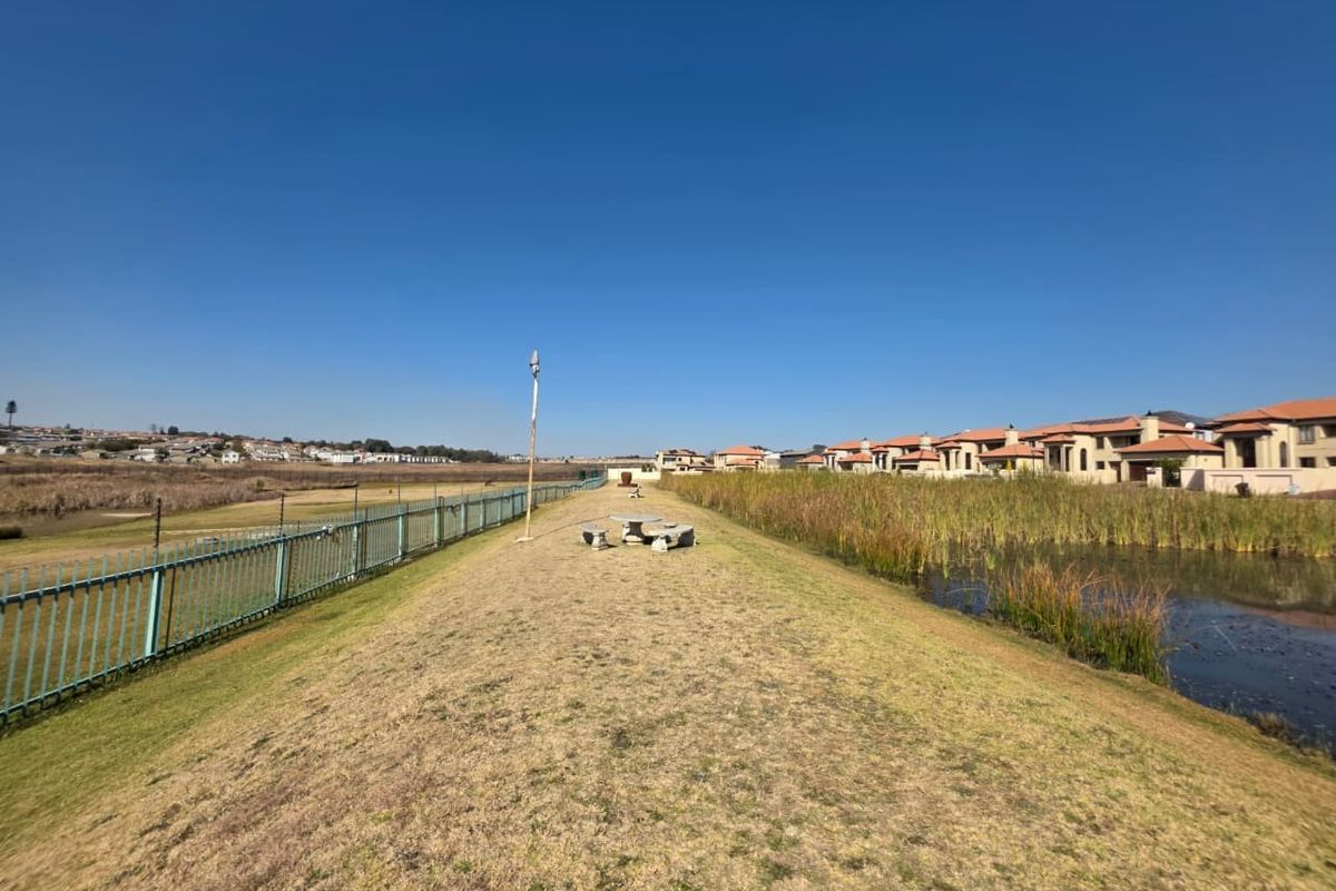 A view of the rear property boundary featuring a landscaped embankment, metal perimeter fencing, and a natural pond area.