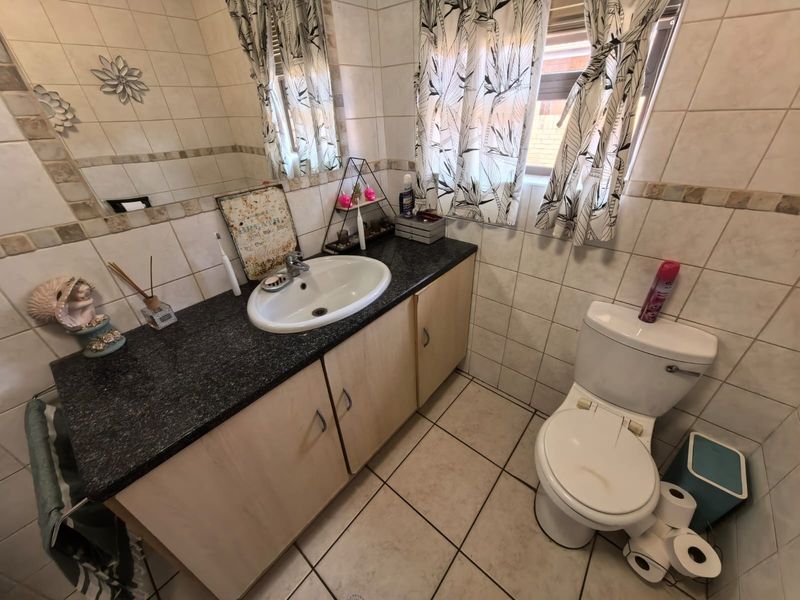 A functional bathroom featuring a vanity cabinet with a granite countertop, ceramic basin, and tiled walls and flooring.