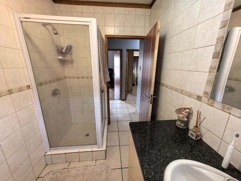 A functional bathroom featuring a glass-enclosed shower, vanity with granite countertop, and neutral wall and floor tiling.