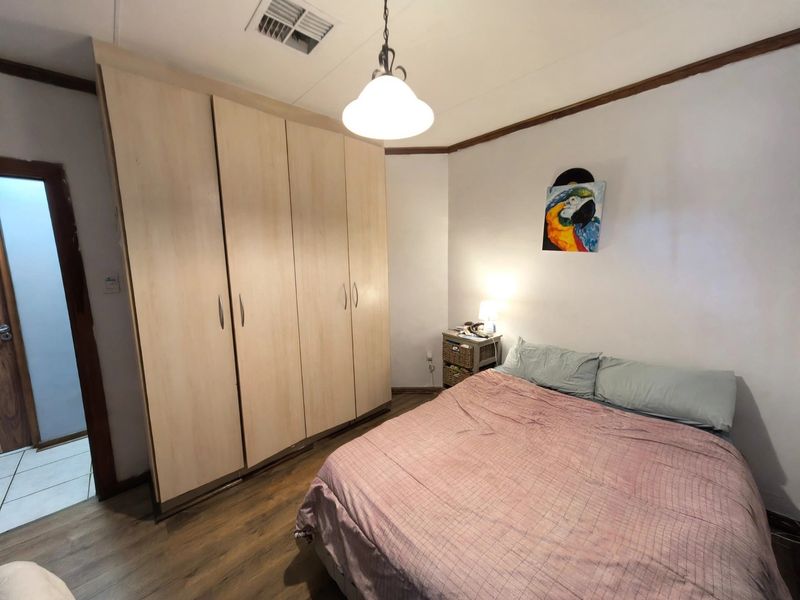 A bedroom featuring laminate flooring, a large built-in wardrobe, and a ducted air conditioning vent.