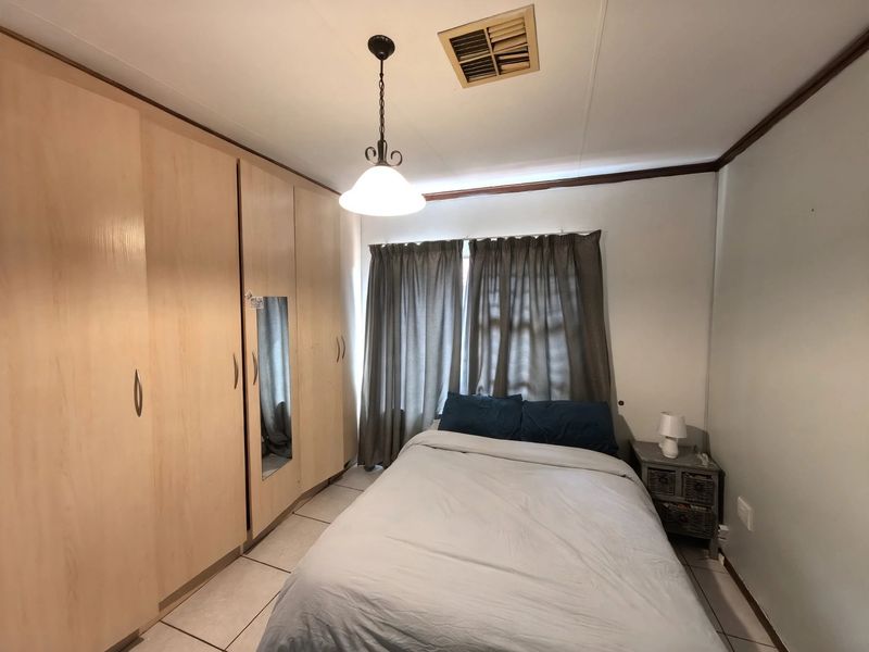 A functional bedroom featuring built-in wooden cupboards, tiled flooring, and a central pendant light fixture.